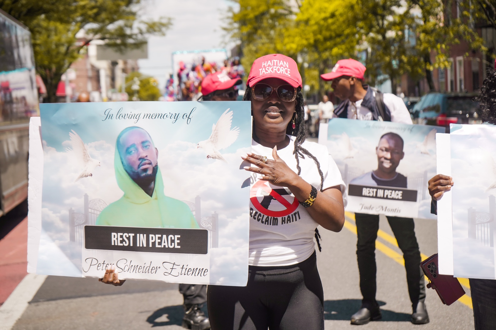 Line of Haitian Taskforce members in 'Stop the Violence, Reclaim Haiti' shirts speaking at an outdoor rally.