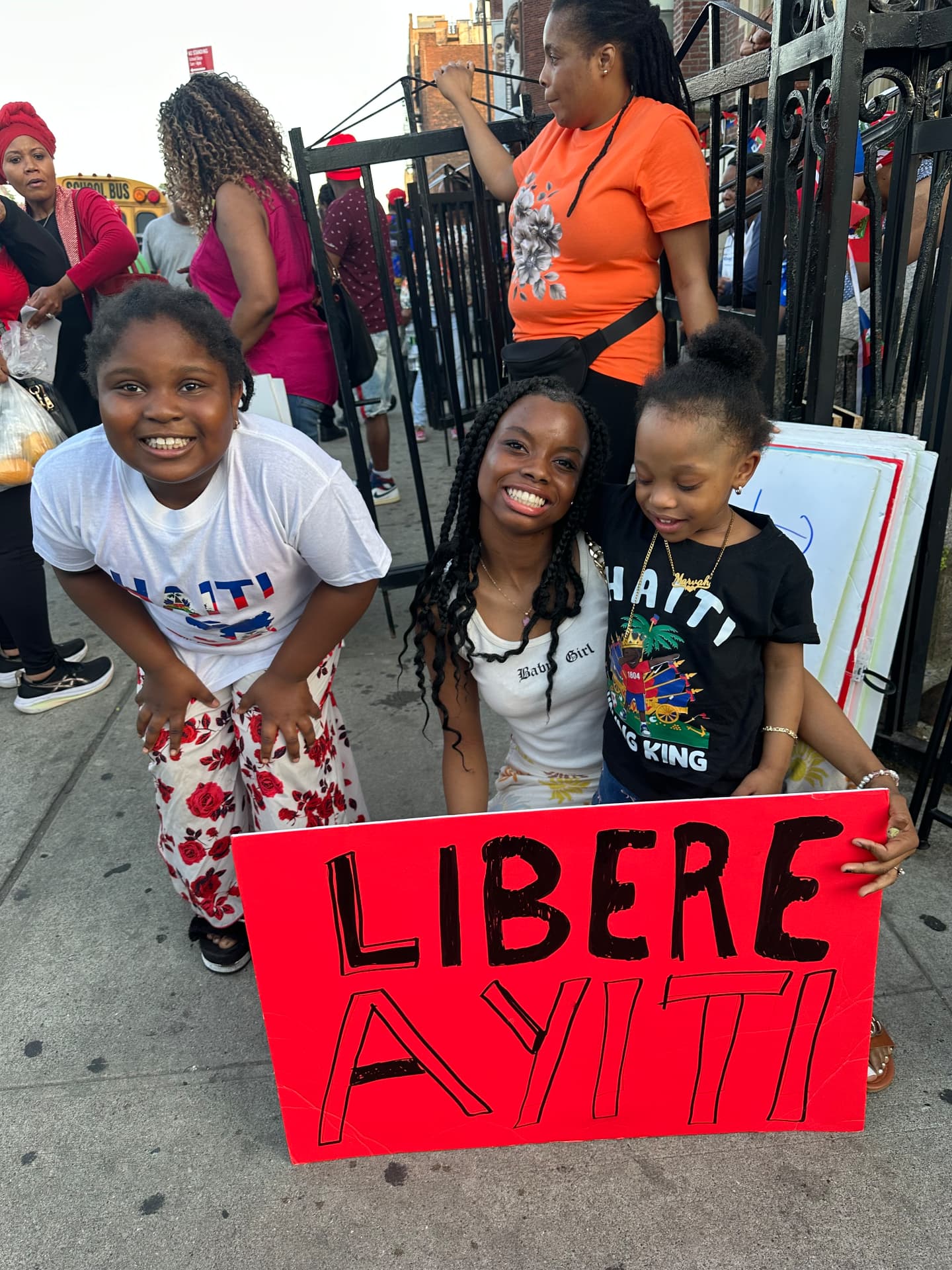 Children smiling behind a bright red 'Libere Ayiti' sign.