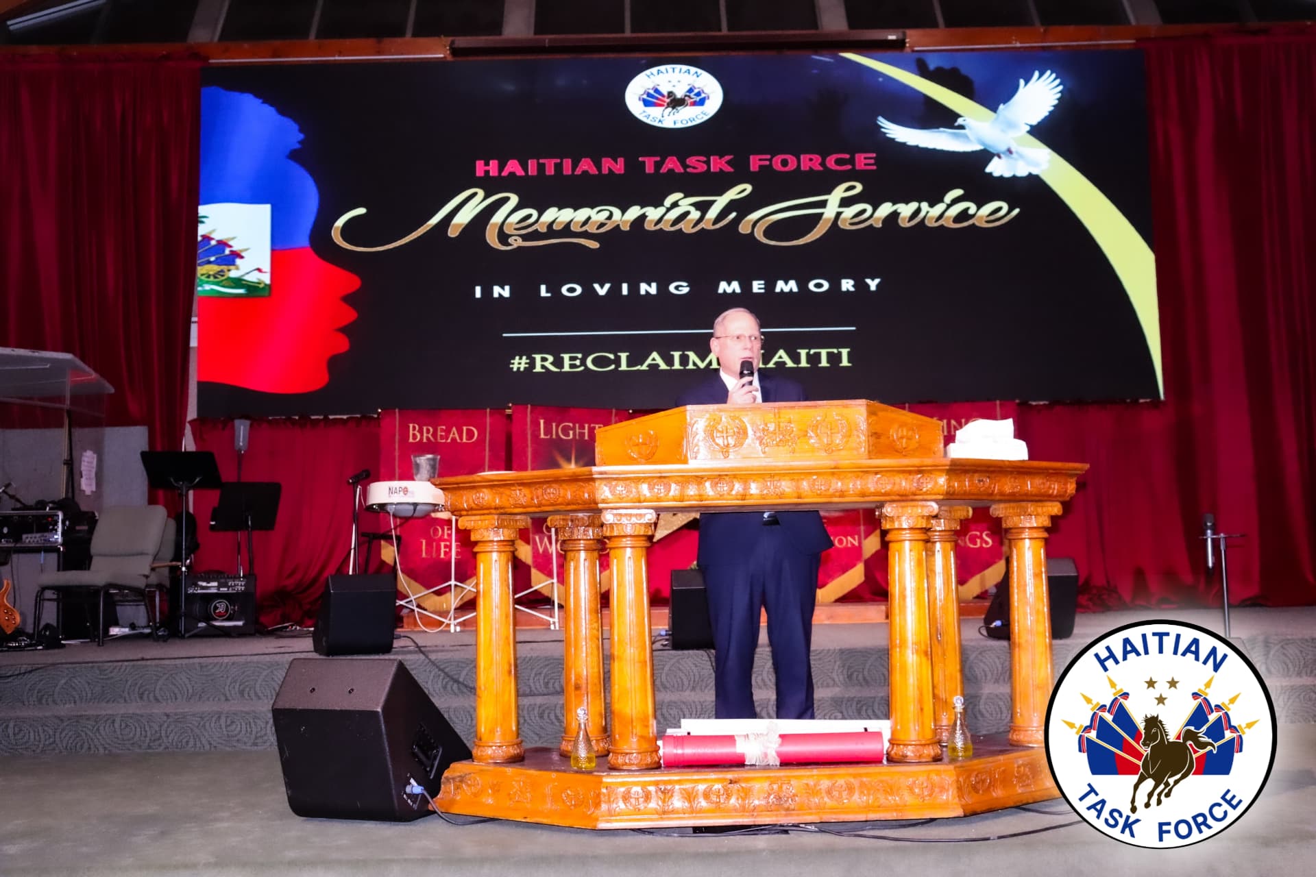 Speaker at the Haitian Task Force Memorial Service beneath a #ReclaimHaiti banner.