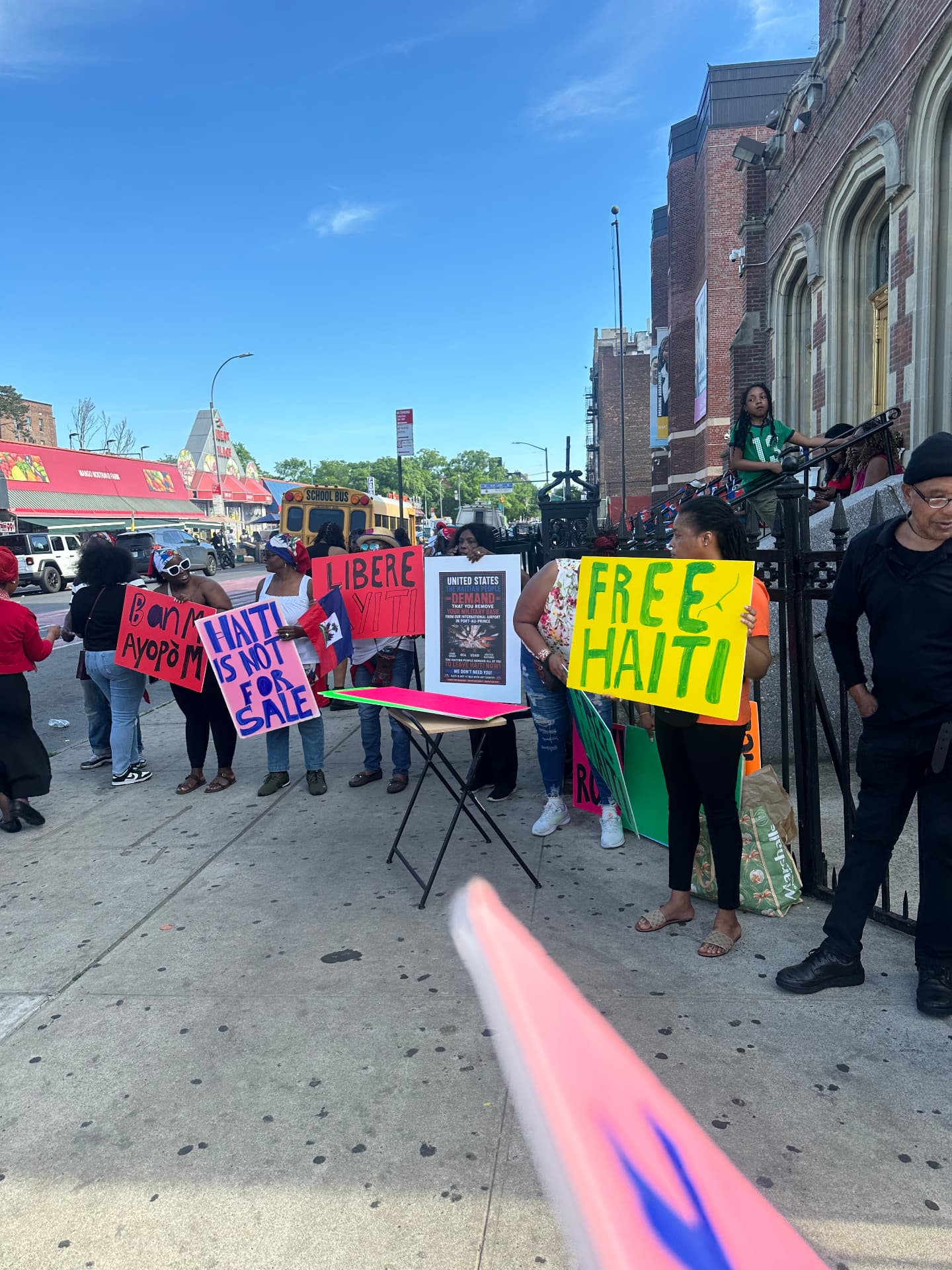 Advocates on a Brooklyn street holding 'Free Haiti' and 'Haiti Is Not For Sale' signs.