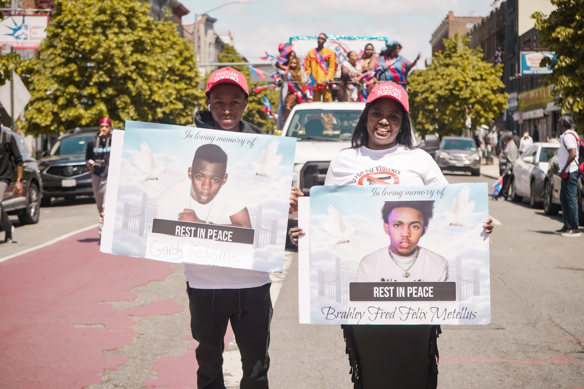 Two Haitian Taskforce members holding 'In loving memory' posters at a parade.